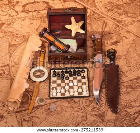 Old compass lying on antique map with treasure chest, knife, money,globe and chess