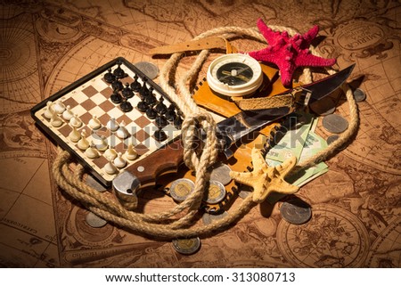 Old compass on antique map with knife, money and chess