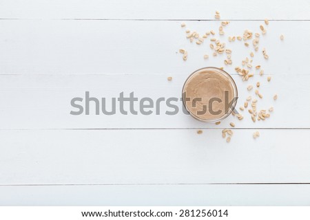White, wooden table top view. On the table are nuts and nut butter in a glass dish.Caloric breakfast.