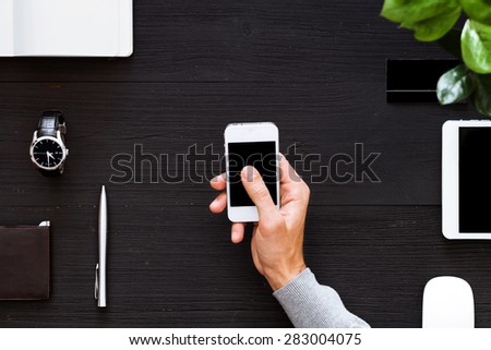 Phone in the hands of a businessman in dark colors. Hand holding mobile smart phone with blank screen.
