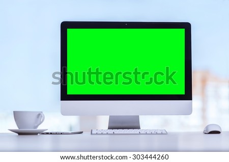 White computer with green screen front view, designed for easy operation. Nearby stands a cup of coffee.