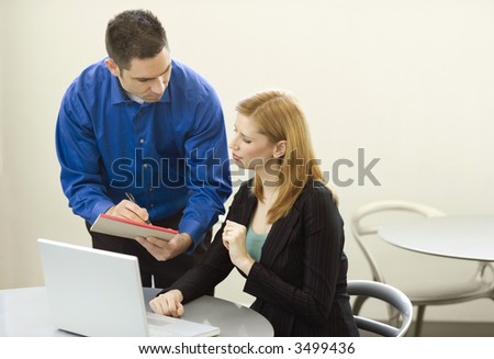 Two business people talk and use a laptop