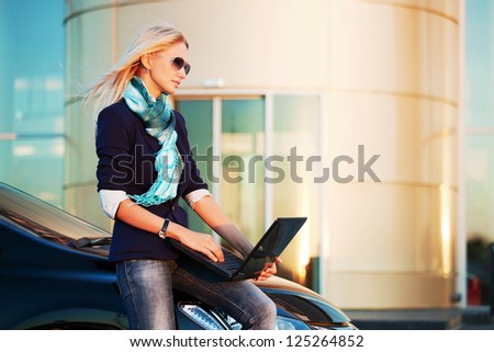 Young businesswoman with laptop sitting on the car