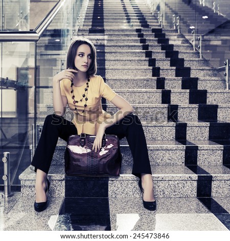 Young fashion business woman sitting on the steps in office interior