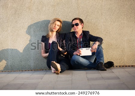 Young fashion couple with tablet computer sitting at the wall