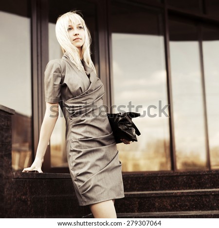 Young fashion business woman with handbag on the steps against office windows