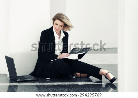 Young business woman with laptop sitting at the wall