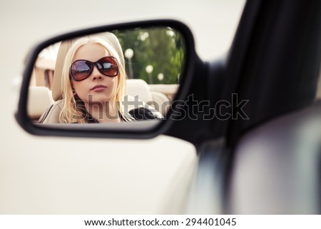 Blond fashion woman in sunglasses looking in the car rear view mirror