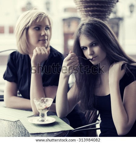 Two young women eating an ice cream at sidewalk cafe