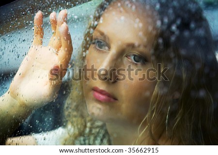 Sad young woman looking through car window with a rain drops.