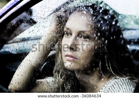 Sad young woman looking through window with a rain drops.