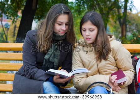Two young teenage students reading in the park.