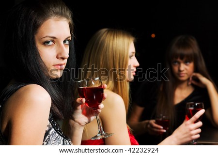 Three young women drinking red wine in a night bar.