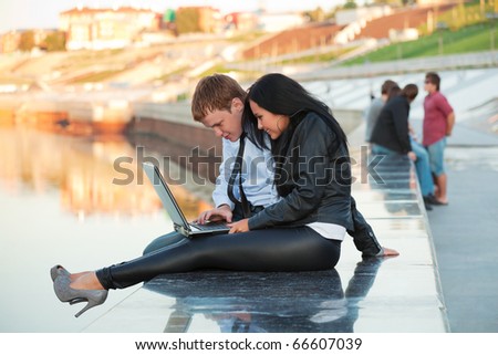 Young couple with laptop on the embankment of river.