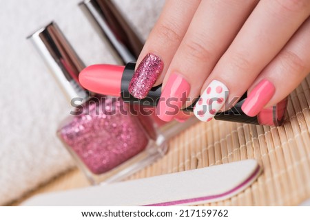 Manicure - Beauty treatment photo of nice manicured woman fingernails holding pink lipstick. Feminine nail art with nice glitter, pink and white nail polish. Selective focus.