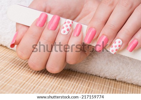 Manicure - Beauty treatment photo of nice manicured woman fingernails holding nail file. Feminine nail art with nice glitter, pink and white nail polish.