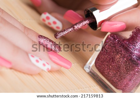 Manicure - Beauty treatment photo of nice manicured woman fingernails. Very nice feminine nail art with nice glitter, pink and white nail polish. Selective focus on glittery fingernail.