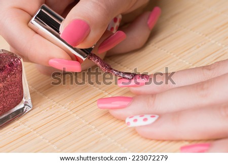 Manicure - Beauty treatment photo of nice manicured woman fingernails. Feminine nail art with nice glitter, pink and white nail polish. Focus is on polish brush and index finger.