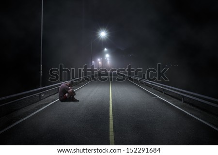 Troubled teenager boy with hidden face sitting in the night street