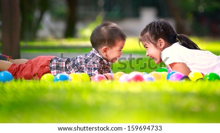 Two children, big syster and her young brother are laying on green grass and smile