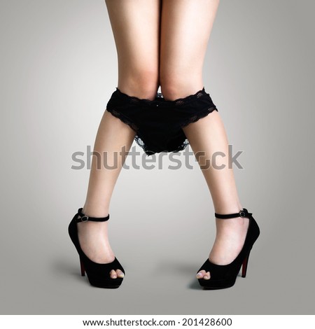 Sexy legs in black bottom high heel shoes pulling panties down on grey background
