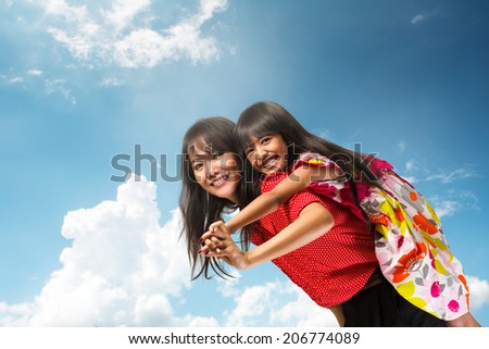 Happy asian mother piggyback ride her daughter over blue sky
