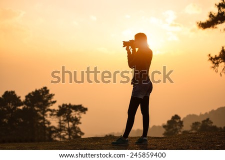 Silhouette female photographer taking a picture with the sun behind