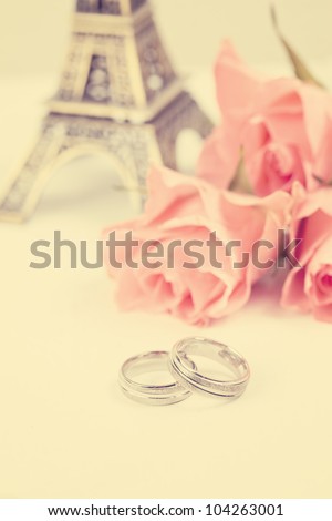 two rings with Eiffel Tower and bouquet of pink roses at background