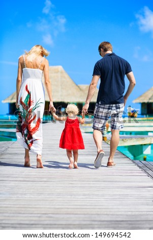 Family of three walking on the bridge towards to water bungalows on Maldives
