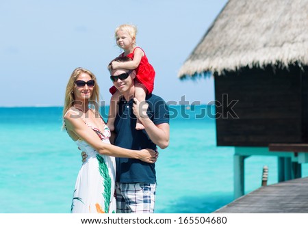 Happy family of three having tropical vacation on Maldives with turquoise water and water bungalow at background