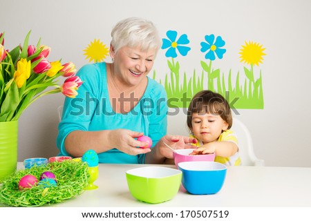 Happy grandmother and grandson color eggs for Easter at home.