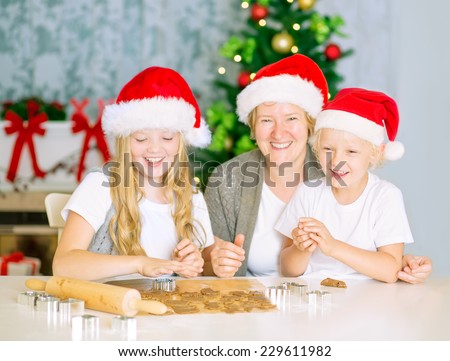 Mom with kids baking Christmas cookies, happy family of three with Santa Hats at home, having fun.