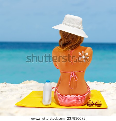 Beach summer holidays. Woman wearing red bikini and beach hat sitting on the mat. Concept of sun protection, model with sunscreen and sunglasses.