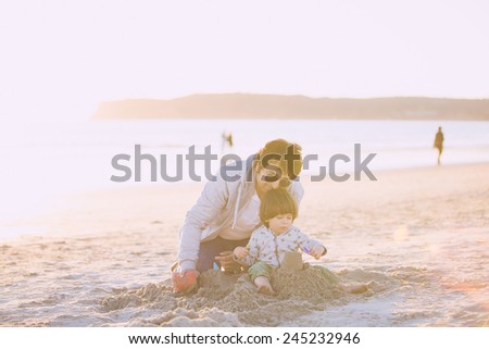 Father and son playing with sand on the beach, kissing and hugging.