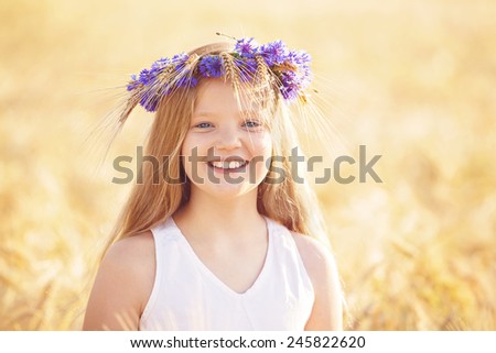 Portrait of beautiful happy blond, Caucasian with blue eyes smiling. Teenager with flowers crown in wheat field.