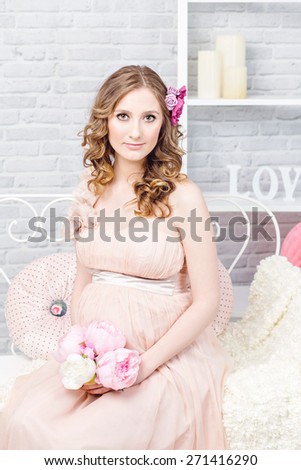 Beautiful elegant pregnant woman with romantic dress, hairstyle and make-up. Studio interior shot.