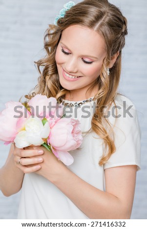 Woman with day bridal make-up and hairstyle, holding bouquet of peonies