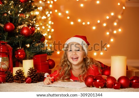 Happy little girl writing a letter to Santa Claus under decorated Christmas Tree, at home