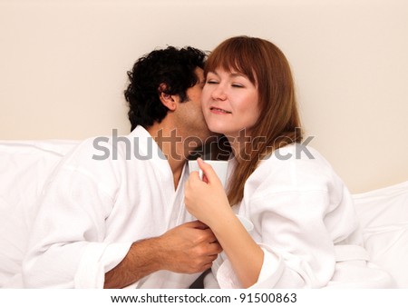 Loving couple having tea or coffee in a bed, kissing and hugging
