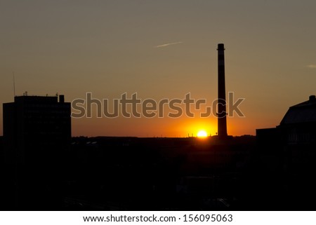 Sunset in Prague behind a tall factory chimney with sun right on the edge of the buildngs. Place: Holesovice area, Prague, Czech Republic