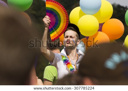 PRAGUE - AUGUST 15, 2015: A man with a rainbow hand fan surrounded by balloons waving the crowd from one of the decorated cars of the fifth Prague Pride 2015. Up to 35,000 people attended the parade.