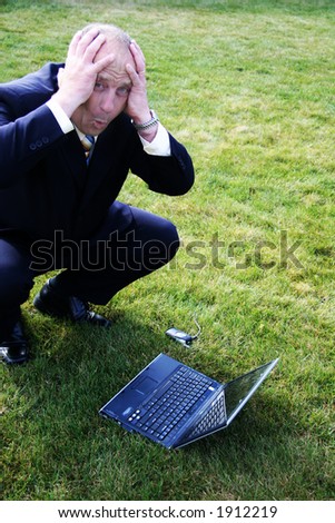 Frustrated Business man outdoors in the grass with hands on head