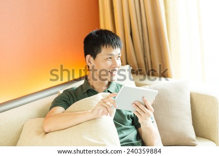 Asian young adult man using tablet and relax on sofa.