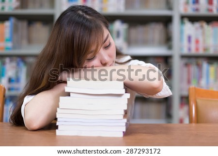 Beautiful asian female student take nap in library during studying stack of books.