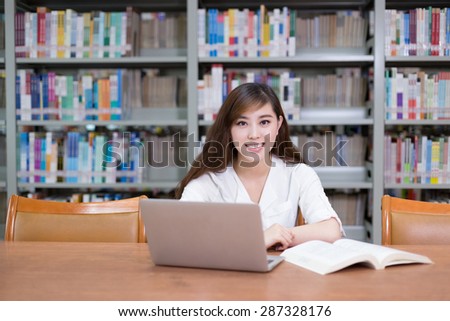 Beautiful asian female student using laptop for study in library with bookshelf background.