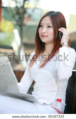 young asian businesswomen reading newspaper and holding mobile phone