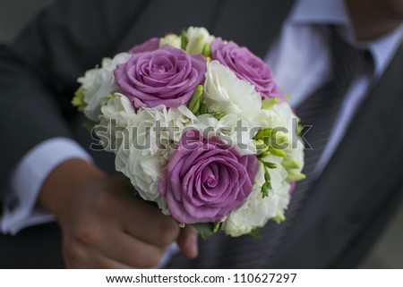 An elegant hand-tied bouquet or bunch of flowers in the hand of a groom or man.