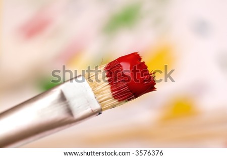 paint brush with red paint over abstract blurred background