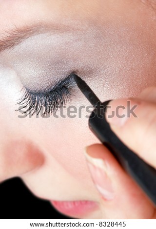 makeup artist tracing eye line with black eyeliner, beautiful girl
