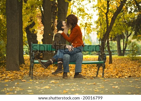 couple kissing on a bench in a park in autumn